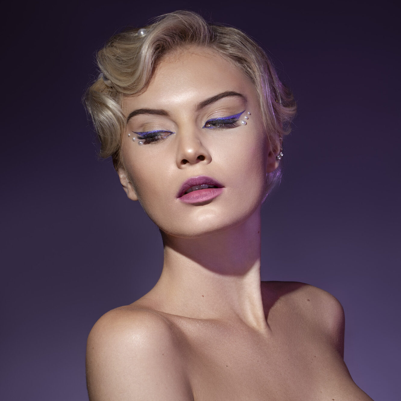 Kvinde med glam makeup, lilla eyeliner og elegant opsat hår i lilla lys