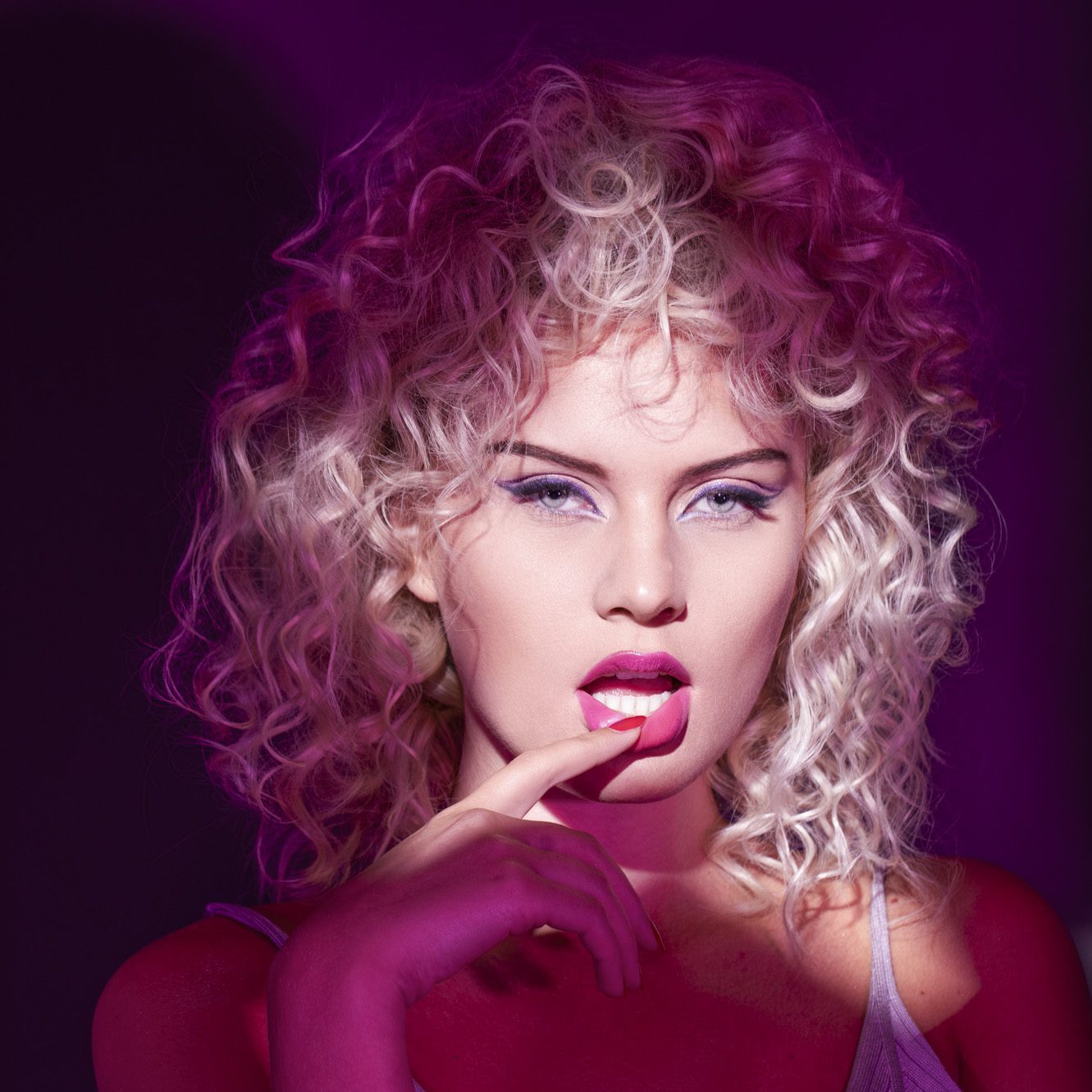 Kvinde med blonde krøller, pink makeup og dramatisk beauty-lys.
