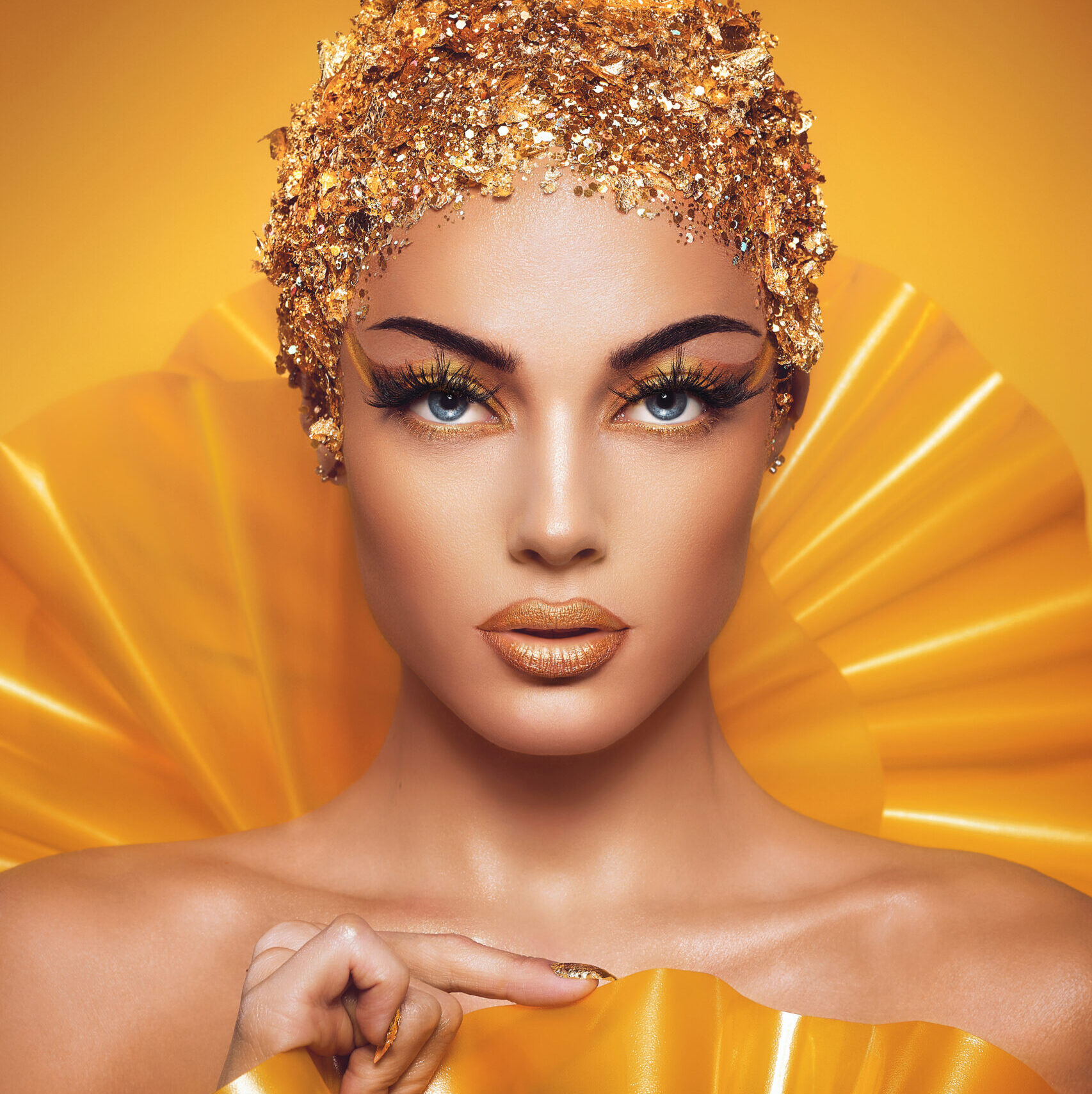 Model med intensiv guldmakeup, guldfolie-stylet hoved og symmetrisk editorial beauty-look.