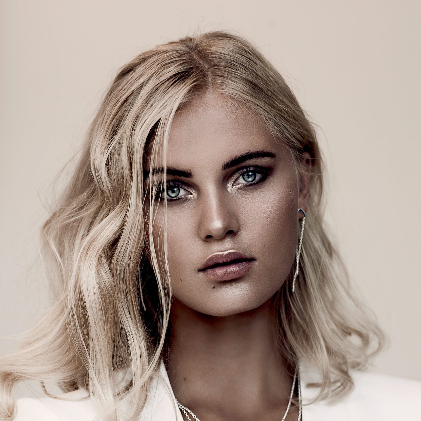kvinde med blond bølget hår, smokey eye makeup og neutral glødende hud i editorial stil