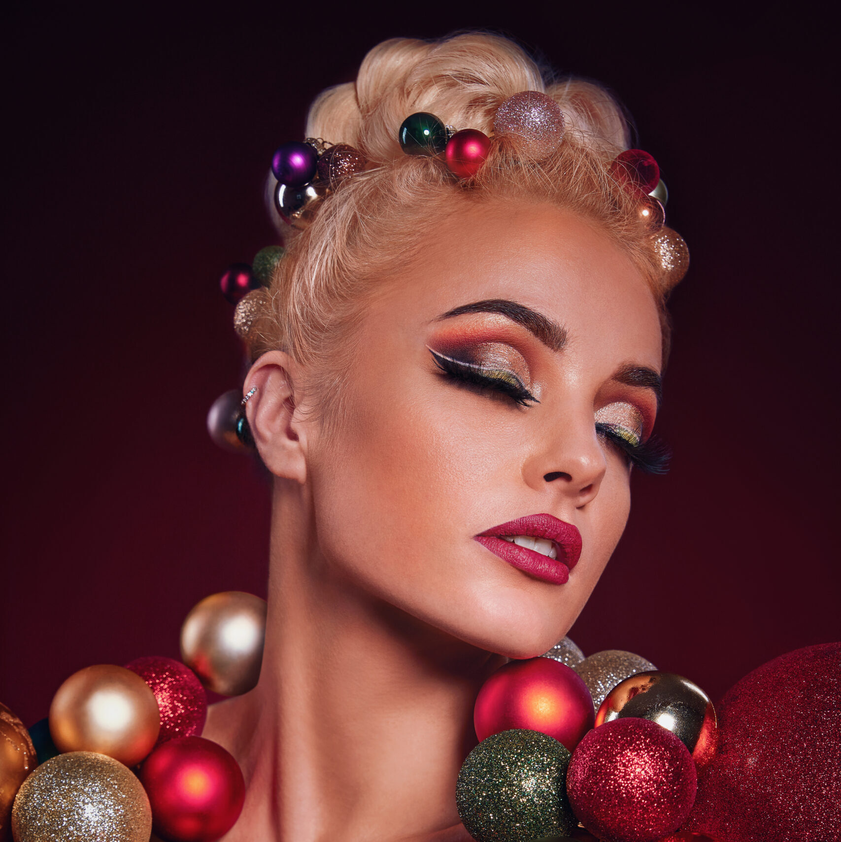 Model med juleinspireret makeup og gyldne, røde og grønne julekugler omkring hoved og skuldre