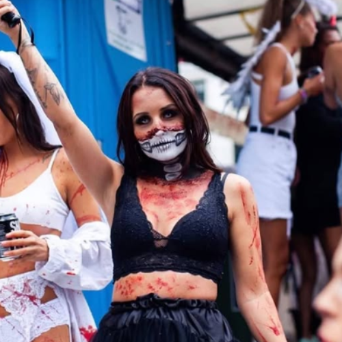 kvinde med blod-effekter på krop og ansigt, sort outfit og skelet-inspireret mundmakeup ved udendørs event