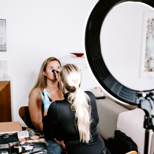 Makeupartist arbejder på kvindes makeup i professionelt setup med ring light og makeupkit.