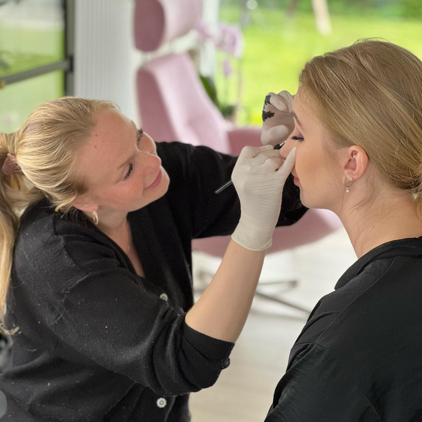 Makeupartist påfører øjenmakeup på kvinde i lyst og professionelt stylingmiljø.