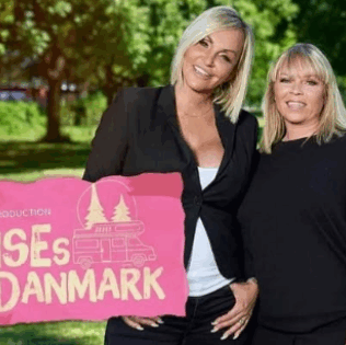 To kvinder med professionel makeup og stylet hår står udendørs i sollys foran et pink skilt.