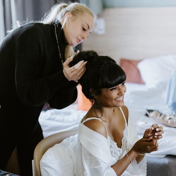 Brud får opsat elegant brudehår af stylist, mens hun sidder i morgenkåbe og forbereder sig.