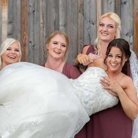 Brudepiger i bordeaux kjoler løfter brud i blondekjole med naturlig brudemakeup og elegant opsat hår.