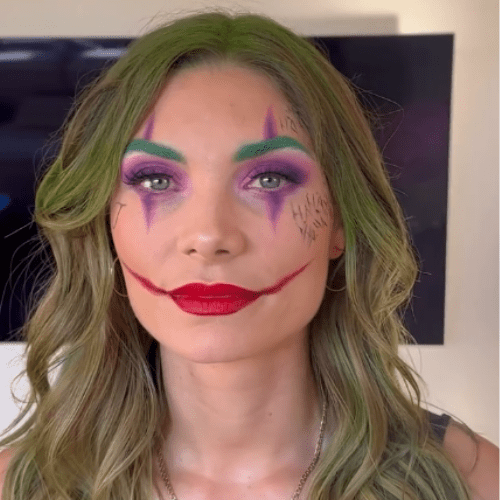 Kvinde med farverig, clown-inspireret makeup med grønne bryn og hår, lilla øjenmakeup og rød overdrevet mundlinje.