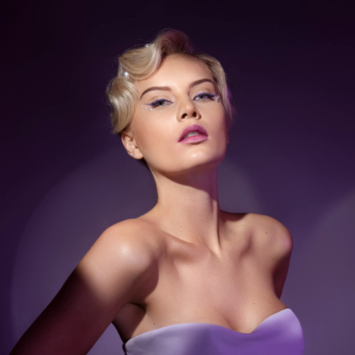 kvinde med sleek kort hårstyling, glødende hud og soft glam makeup i lilla editorial lys